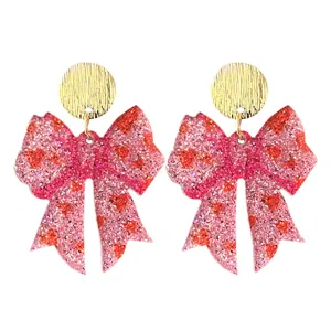 Gros plan de boucles d'oreilles nœud à paillettes roses étincelantes avec clous ronds dorés.