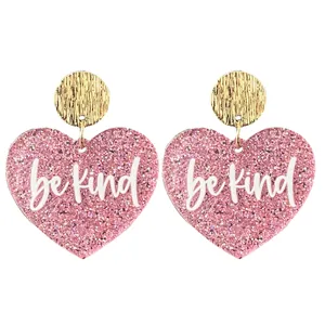 Boucles d'oreilles cœur pailleté rose gros plan avec disque doré et inscription be kind.