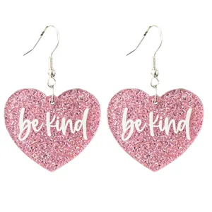 Gros plan détaillé de boucles d'oreilles pendantes cœur pailleté rose avec texte be kind.