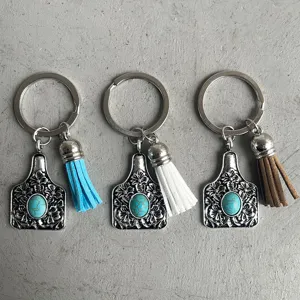 Close-up detail of western cowboy style turquoise alloy cattle tag keychain with leather tassel.