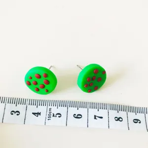Grüne runde Ohrstecker aus Fimo im Detail mit Maßband für den perfekten Größenvergleich.
