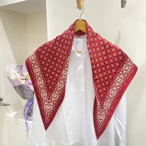 Vista dettagliata della sciarpa triangolare in seta con motivo cachemire rosso su camicia.