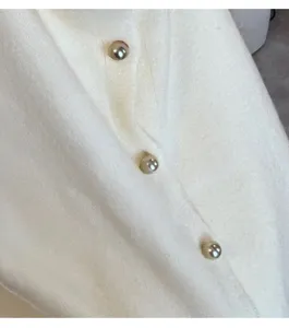 Close up of white knit sweater garment detail featuring three elegant spherical pearl buttons.