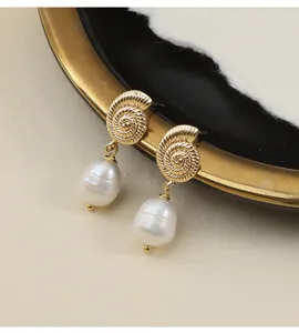 Detailaufnahme von goldenen Muschel-Ohrringen mit hängenden Barockperlen auf schwarzem Tablett.