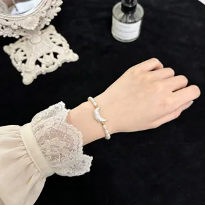 Nahaufnahme des Perlenarmbands mit Mondsichel-Anhänger, elegante Detailansicht am Handgelenk.