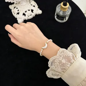 Nahaufnahme eines süßen Naturperlen-Armbands mit Mond-Anhänger und eleganter Spitzenärmel-Optik.