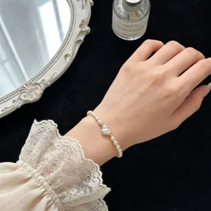 Perlenarmband Detail mit Barockperle und Goldperle am Handgelenk vor schwarzem Hintergrund.