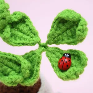 Close-up detail of handmade crochet four leaf clover potted plant with cute wooden ladybug.