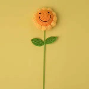 Detailed view of handmade crochet sunflower flower with cute smile face and green stem.