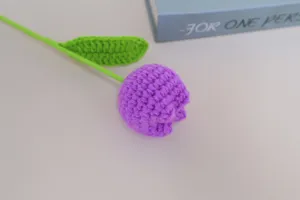 Close-up of handmade crochet purple tulip with green stem and leaf, delicate home decor detail.