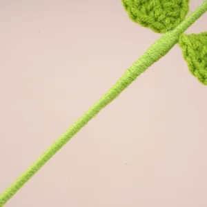 Close-up detail of handmade crochet green flower stem and knitted leaves, soft wool texture.