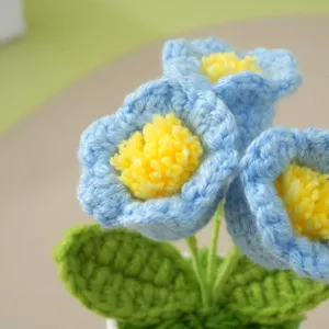 Nahaufnahme handgemachter Häkel-Blumenstrauß in Blau mit gelber Mitte und grünen Blättern.