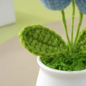 Nahaufnahme Detail der handgefertigten Häkel-Topfblume mit grünen Blättern im weißen Topf.