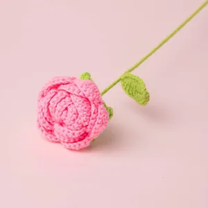 Nahaufnahme einer handgehäkelten rosa Rose mit grünem Stiel und einzelnem Blatt, Detail.