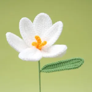 Handcrafted white crochet flower detail showing delicate petals, yellow stamen, and green leaf.
