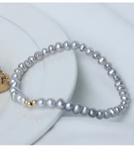 Nahaufnahme Detail des grauen Süßwasserperlen Armbands mit goldenen Perlen im eleganten Stil.