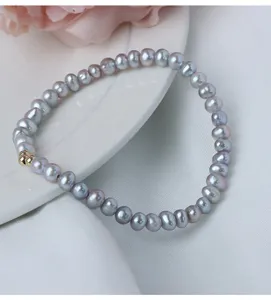 Nahaufnahme eines grauen Süßwasserperlenarmbands mit goldenem Perlendetail, zart und schick.
