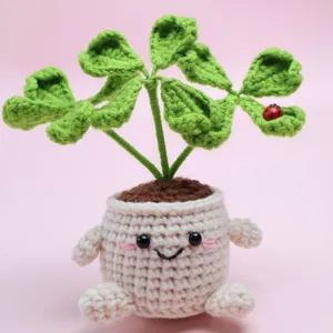 Handmade crochet potted plant with cute smiling face pot and green clover leaves desktop decor.