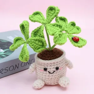 Detailed shot of handmade crochet four-leaf clover potted plant with cute smiling pot and ladybug.