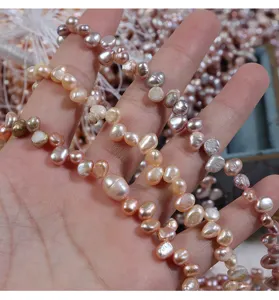 Nahaufnahme von mehrfarbigen unregelmäßigen Barock-Süßwasserperlen auf der Hand für Schmuck.