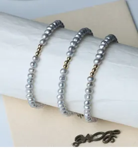 Detailaufnahme von grauen Süßwasserperlenarmbänder mit goldfarbenen Perlen auf weißem Zylinder.