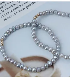 Nahaufnahme Detail des grauen Perlenarmbands mit vergoldeten Perlen auf Papierhintergrund.