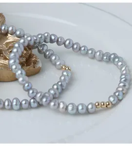 Nahaufnahme eines grauen Süßwasserperlenarmbands mit goldenen Perlen, eleganter Stil.