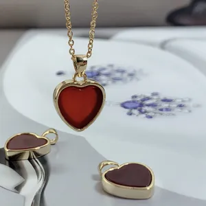 Detailed shot of a stylish gold necklace with a natural red agate heart pendant and extra charms.