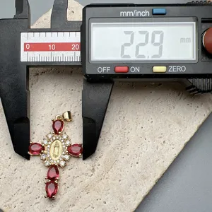 Dettaglio del pendente a croce dorata che mostra la misura esatta con zirconi rossi.