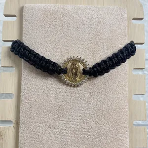 Close-up detail of black braided rope bracelet featuring gold Guadalupe pendant with sparkling zircon.