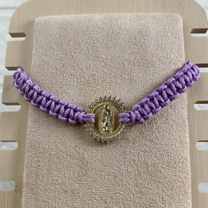 Close-up detail of the purple braided rope bracelet featuring a gold Guadalupe rhinestone charm.