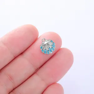 Close-up of a silver shell charm encrusted with blue rhinestones on fingers for DIY jewelry.