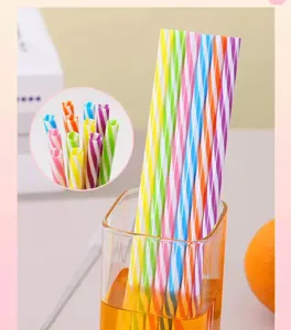 Detail view of colorful reusable plastic striped drinking straws in a glass with orange fruit.