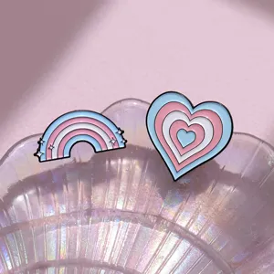 Close-up of pastel enamel pins featuring a rainbow and layered heart design on a shell tray.