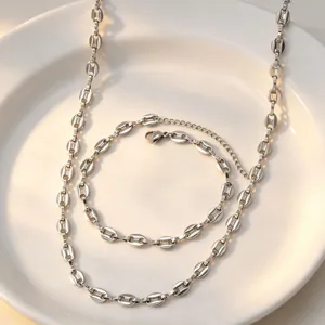 Close-up detail view of silver coffee bean link chain necklace and bracelet on white plate.
