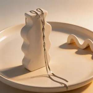 Close-up detail of a minimalist silver snake chain necklace draped gracefully on white ceramic.