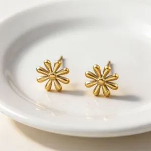 Close-up detail of exquisite gold-plated daisy flower stud earrings on white plate background.