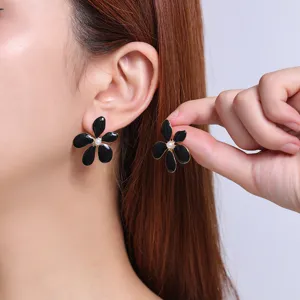 Close-up detail of elegant black enamel flower stud earrings with a central pearl accent.