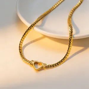 Detailopname van de gouden platte slangenketting met een holle hartvormige hanger erop.