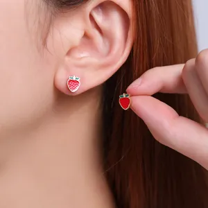Close-up detail of cute red strawberry stud earrings worn on ear, showing delicate enamel glaze.