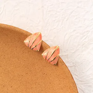 Close-up of geometric triangle earrings with pink enamel and gold lines on a round dish.