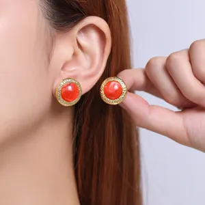 Close-up detail of stylish round red and gold earrings worn on ear, fashion jewelry piece.