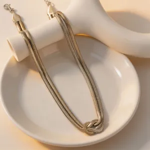 Primo piano di un'elegante collana a catena serpentina piatta dorata con nodo unico.