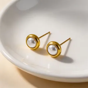 Detail shot of minimalist gold bezel pearl stud earrings in a white ceramic dish.