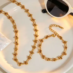 Gros plan détaillé d'un collier et d'un bracelet de chaîne à nœuds en acier inoxydable dorés.