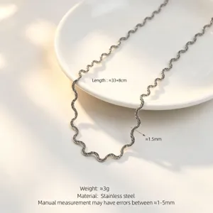 Detail shot of wavy stainless steel necklace on white plate, featuring unique ripple design.