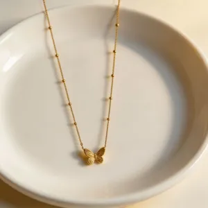 Gold butterfly pendant necklace detail shot on a white plate elegant jewelry piece