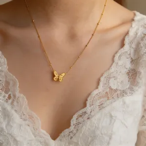 Close-up detail of a delicate gold butterfly pendant necklace worn with white lace dress.