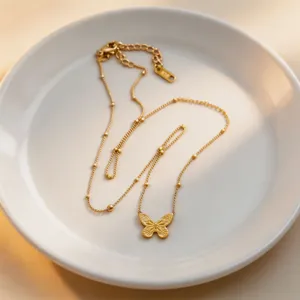 Close-up detail of the delicate gold butterfly necklace with bead accents on white plate.
