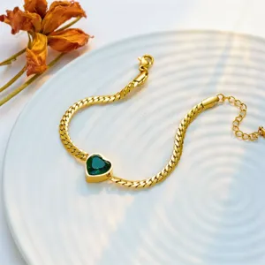Gold-tone cuban chain bracelet detail featuring a sparkling green heart crystal pendant.